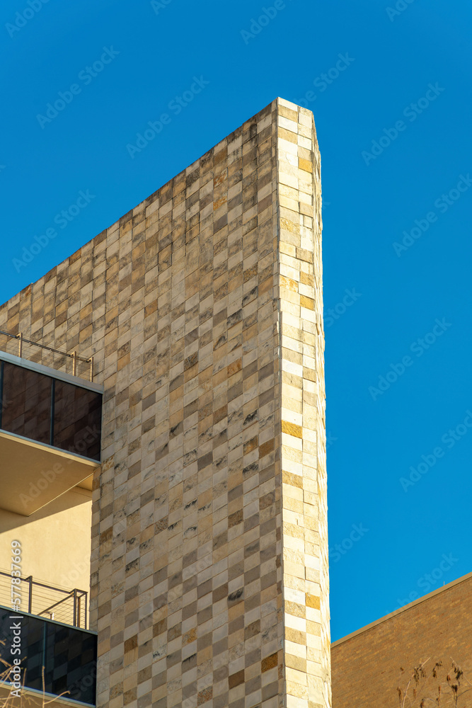 Decorative building facade with stones and rock tiles in late afternoon sun and shade with metal balconies and walkways