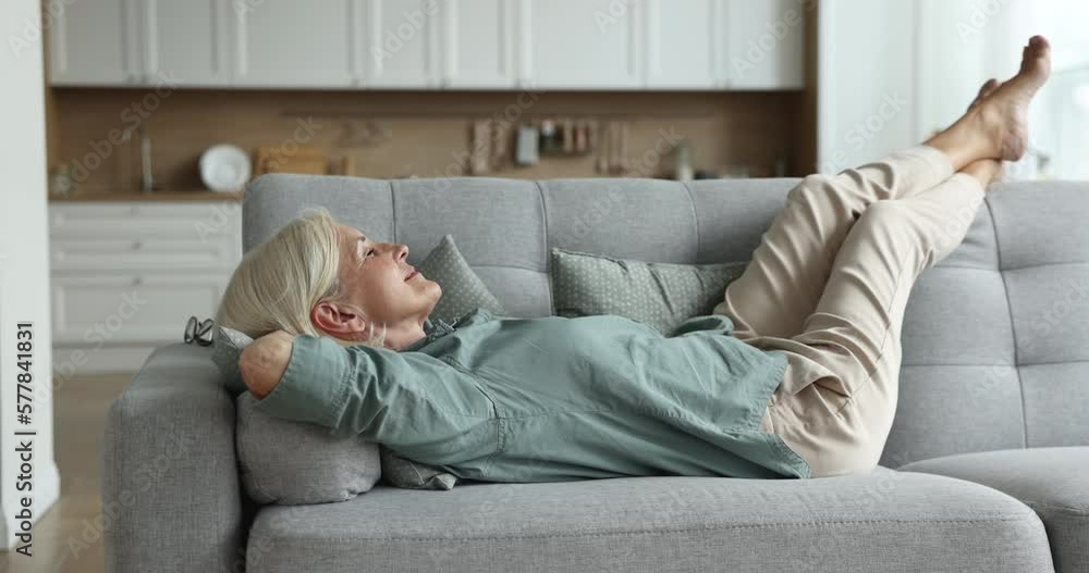 Peaceful retiree, serene mature woman in casual clothes lying down, relaxing on comfortable sofa, breath fresh air inside cozy living room, take break on weekend, resting looking carefree feels good Peaceful retiree, serene mature woman in casual clothes lying down, relaxing on comfortable sofa, breath fresh air inside cozy living room, take break on weekend, resting looking carefree feels good