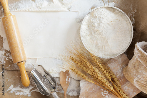 Fotografiet Flour in a bowl and wheat grains with wheat ears on the table, paper background
