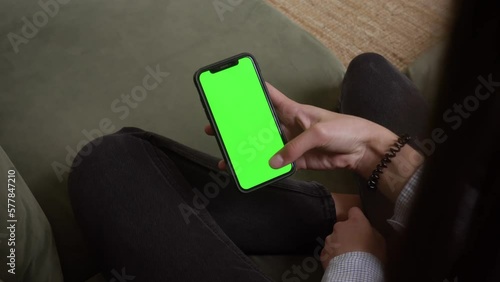 Close up of using smartphone with green screen and scrolling while sitting in room. Female holding black mobile phone with chroma key in hand, tech concept. Video 4K.
