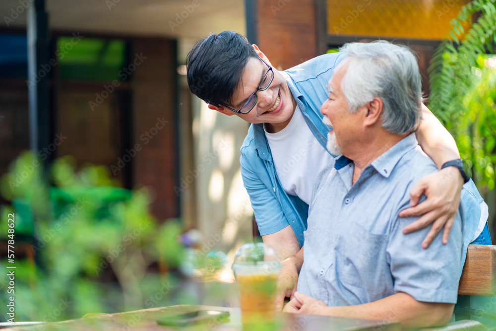 Asian man surprise hugging elderly father from back at outdoor garden cafe restaurant on summer vacation. Family relationship, holiday celebrating, father's day and old people health care concept Asian man surprise hugging elderly father from back at outdoor garden cafe restaurant on summer vacation. Family relationship, holiday celebrating, father's day and old people health care concept