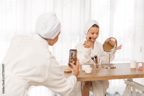 Little girl and her mom in bathrobes recording makeup tutorial at home photo