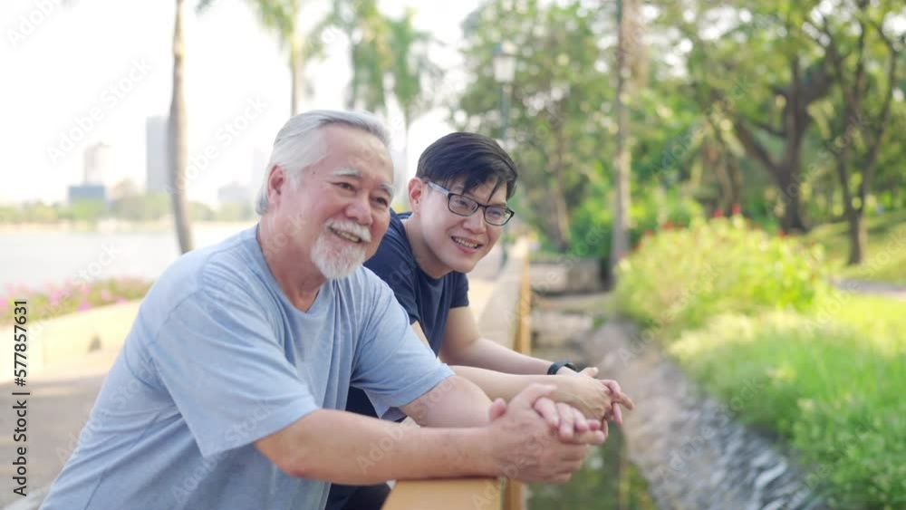 Asian adult son and elderly father looking beautiful nature during jogging exercise together at park. Retired man enjoy outdoor sport workout. Family relationship and older people health care concept. Asian adult son and elderly father looking beautiful nature during jogging exercise together at park. Retired man enjoy outdoor sport workout. Family relationship and older people health care concept.