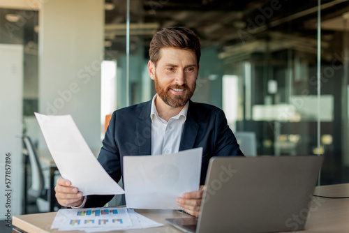 Canvas Print Busy male entrepreneur working with laptop and documents in office, checking com