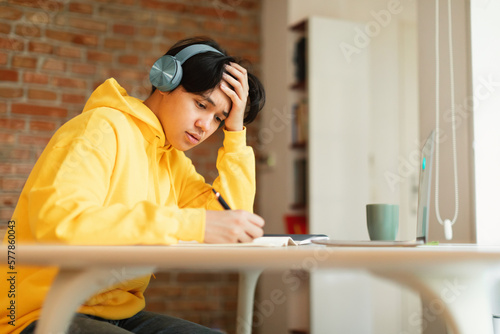 Japanese Teenager Boy Learning Wearing Headphones Taking Notes At Home