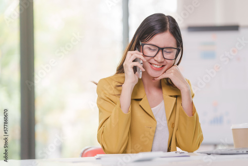 Female attractive asian banker accountant wearing yellow formal suit calculate the cash bill of audit and balance sheet working with quarterly reports of company. call a mobile phone