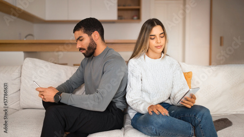 Offended sad millennial arabic guy ignores european lady, watch video on phone in room interior, panorama