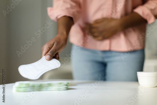 African american woman feeling pain during menstrual cycle and taking daily sanitary pad from table  selective focus