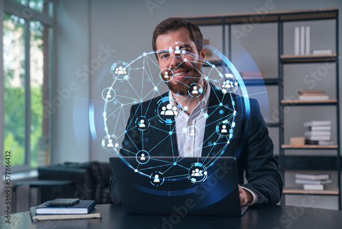 Smiling businessman in formal wear working on laptop at office workplace with smartphone and notebooks. Concept of successful business deal, agreement. Social network icons.