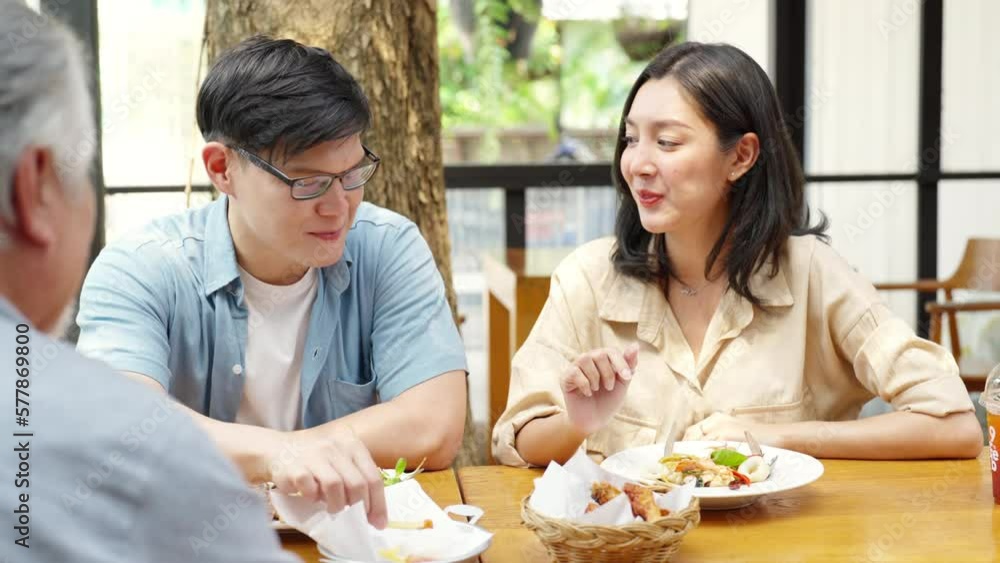 Happy Asian family couple and elderly father having lunch eating food together at cafe restaurant on summer holiday vacation. Family relationship, fathers day and older people health care concept. Happy Asian family couple and elderly father having lunch eating food together at cafe restaurant on summer holiday vacation. Family relationship, fathers day and older people health care concept.