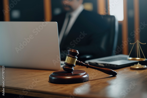 A close up of a gavel of justice with a judge working on a laptop inside an office.