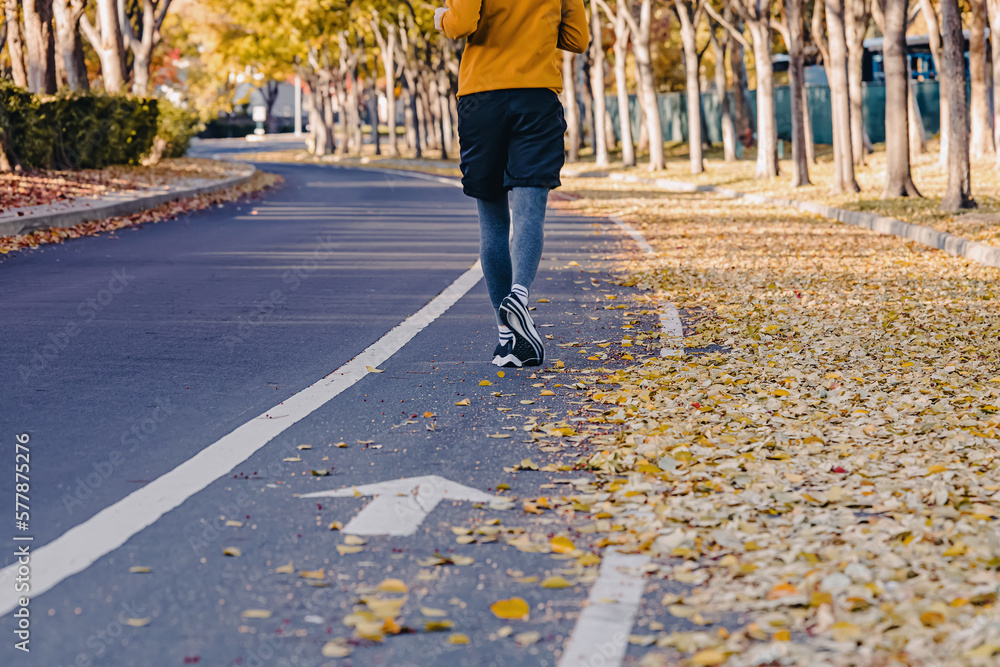 Fototapeta premium Feet of unrecognizable man jogging outdoors in the fall. Yellow leaves on the street,