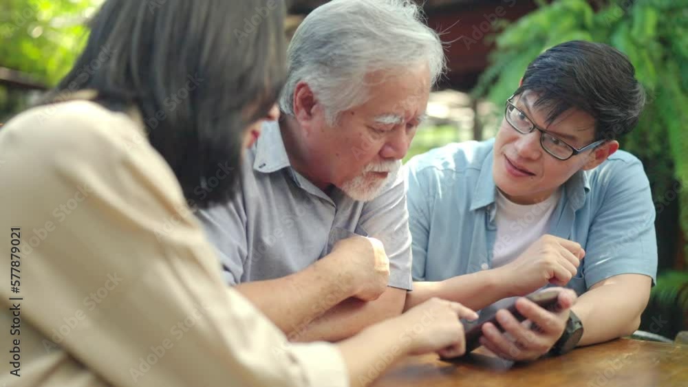 Happy Asian couple teaching elderly father using mobile phone application during having lunch together at restaurant on summer vacation. Family relationship older people mental health care concept. Happy Asian couple teaching elderly father using mobile phone application during having lunch together at restaurant on summer vacation. Family relationship older people mental health care concept.