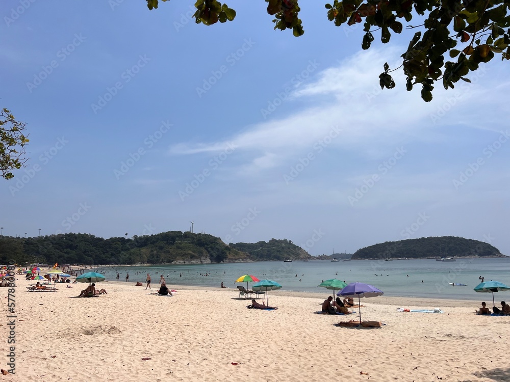Fototapeta premium Thai beach Nai Harn. Yellow sand and the sea Sunbathing people on the beach under an umbrella.