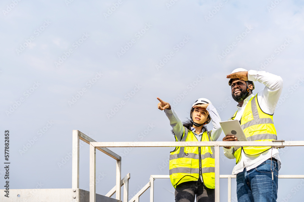 Front view of african american man and woman engineers in uniform discuss use tablet stand near wind turbines ecological energy industry, Environmental friendly for the future Front view of african american man and woman engineers in uniform discuss use tablet stand near wind turbines ecological energy industry, Environmental friendly for the future