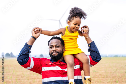 Black african father engineer holds his daughter in his arms at the wind turbines with great freedom. Concept of environmental engineering, renewable energy and love for nature and for the family
