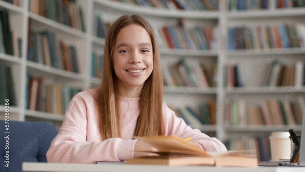 Happy student. Young beautiful lady sitting in campus library and smiling widely to camera, tracking shot, free space Happy student. Young beautiful lady sitting in campus library and smiling widely to camera, tracking shot, free space