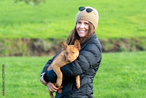 girl on a farm holding a puppy dog in her arms, tan kelpie puppy