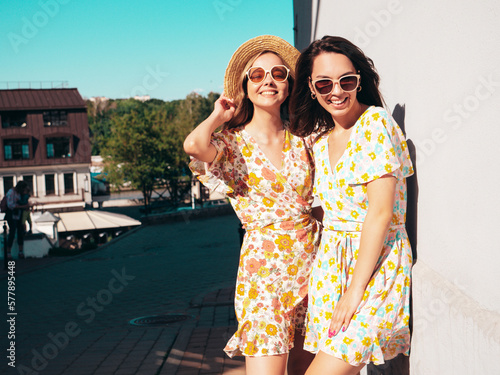 Two young beautiful smiling hipster female in trendy summer dresses  clothes. Sexy carefree women posing in the street. Positive models having fun, talking, chatting. Going crazy. Cheerful and happy © halayalex