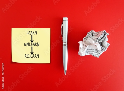 Pen, crumpled paper and note paper on red background with handwritten text Learn Unlearn Relearn - means knowing to discard learned outdated knowledge skills information and ready to relearn new ones photo