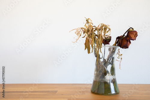 Old dead wilted 
flowers in glass vase on wooden table photo