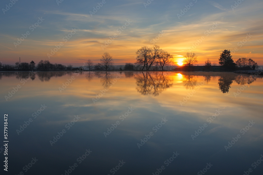 Calm reflection sunrise on pond in winter. Czech tranquil landscape background
