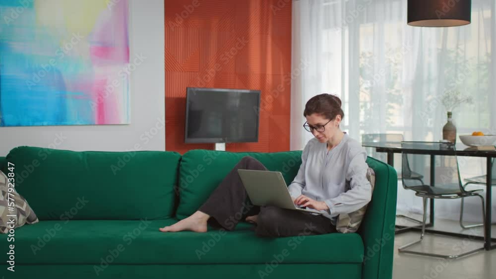 Young woman sitting on couch using laptop looking at screen typing message Young woman sitting on couch using laptop looking at screen typing message