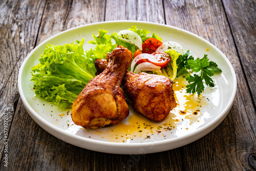 Barbecue chicken drumsticks with lettuce and tomatoes on wooden table
