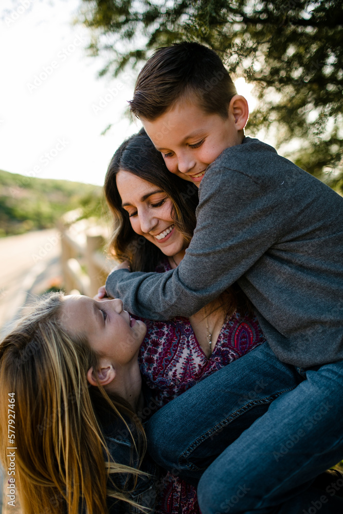 Son Hugging Mom While Mom and Daughter Smile at Each Other in SoCal Son Hugging Mom While Mom and Daughter Smile at Each Other in SoCal