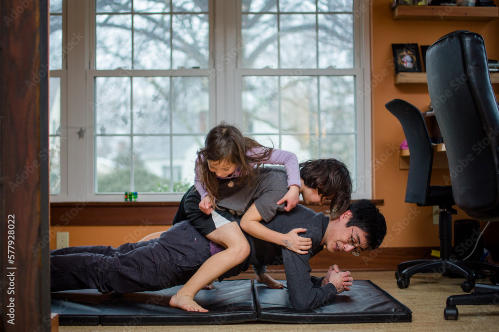 A father holds a yoga position with two children piled on his back A father holds a yoga position with two children piled on his back