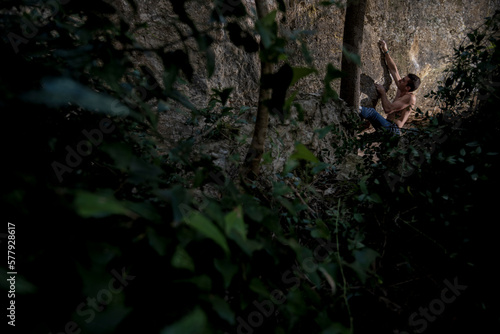 Athletic climber sending a difficult bouldering problem in forest.