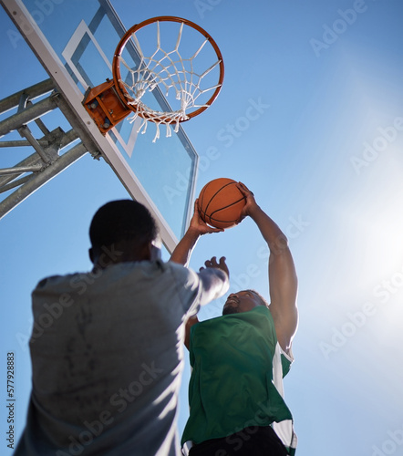 Basketball player, low angle and competition games on blue sky background of outdoor sports, fitness and energy for goals, performance and action. Basketball hoop, friends and men, court and training