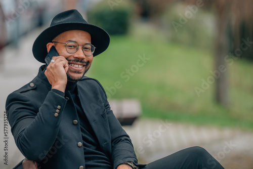 latin man with hat talking on mobile phone sitting on a bench outdoors