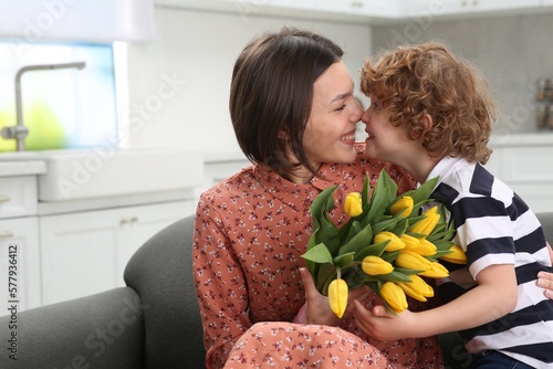 Little son congratulating his mom with Mother`s day at home. Woman holding bouquet of yellow tulips