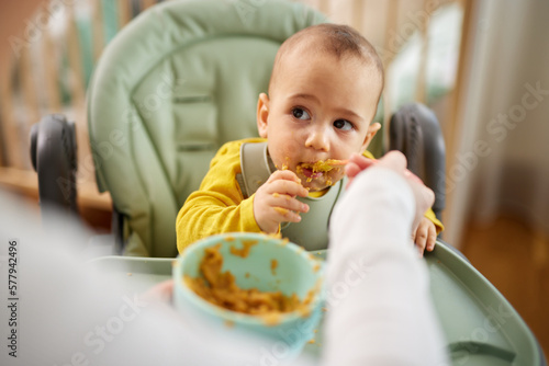 Mother spoon feeding her baby son at home