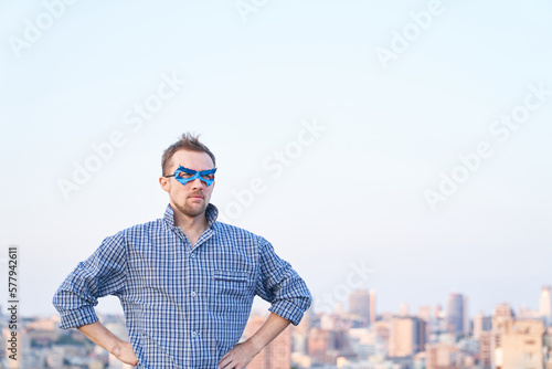 Adorable caucasian male in sleep wear and superhero blue mask standing outdoor with serious face. Urban view on background. High quality image