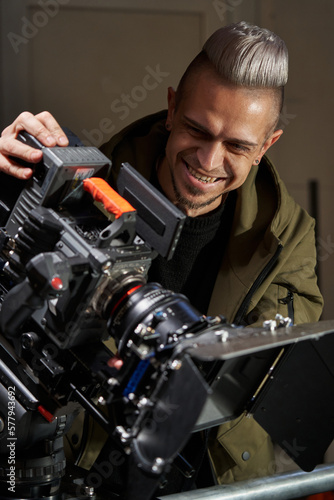 caucasian videographer filming and laughing while standing behind a professional movie camera on the set File not selected