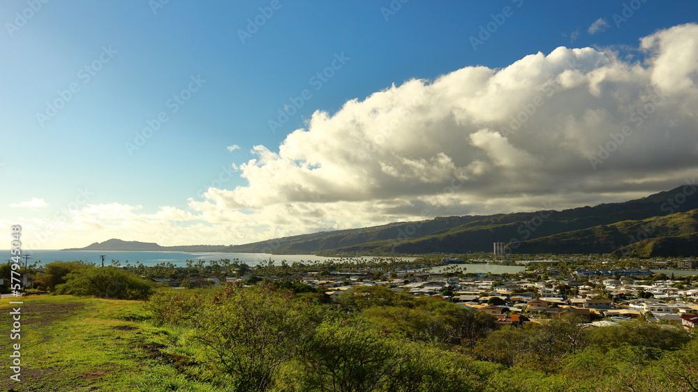 Scenic panoramic view over Hawaii Kai suburbs and surrounding mountain landscape as clouds build on a sunny day, with Diamond Head in the distance. Near Honolulu, Hawaii.