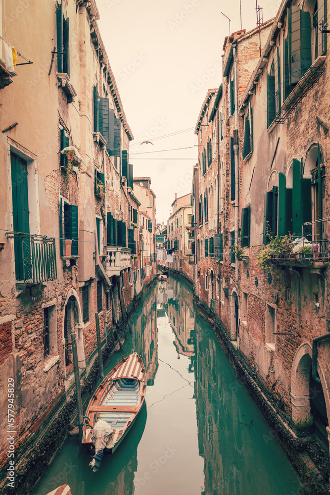 Old narrow canal in Venice with green water, medieval houses on the sides and boats (vintage photo effect)