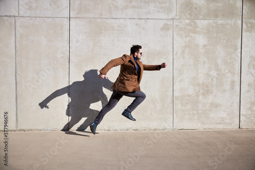 Casual man running in urban setting wearing coat on sunny spring day