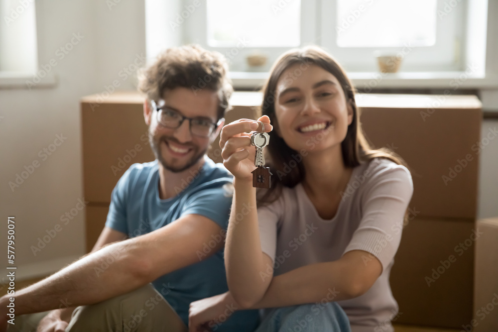 Happy young couple showing keys from hew home together, looking at camera, smiling, sitting at cardboard relocation boxes, feeling happy, enjoying moving into new flat, apartment, house Happy young couple showing keys from hew home together, looking at camera, smiling, sitting at cardboard relocation boxes, feeling happy, enjoying moving into new flat, apartment, house