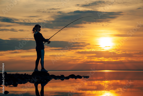 Woman fishing on Fishing rod spinning at sunset background. © Andrei Armiagov