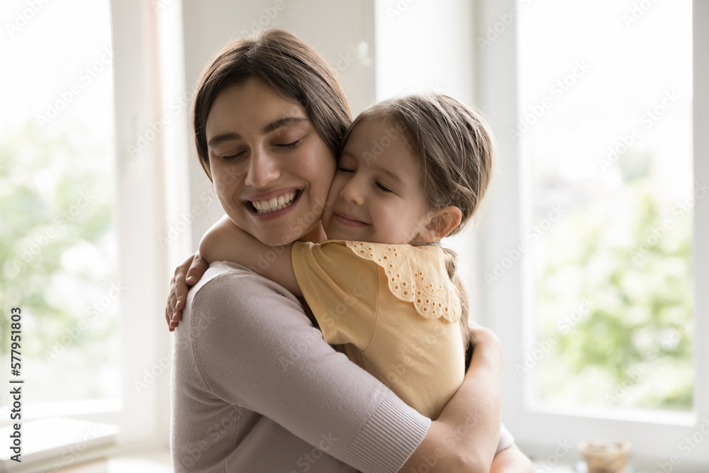 Cheerful happy young mother holding daughter kid in arms, tightening with cheek touches and closed eyes, hugging girl with love, tenderness, devotion, enjoying motherhood, closeness Cheerful happy young mother holding daughter kid in arms, tightening with cheek touches and closed eyes, hugging girl with love, tenderness, devotion, enjoying motherhood, closeness