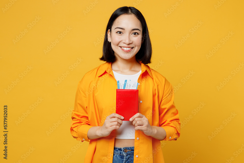 Young smiling happy woman wear summer casual clothes hold passport ticked isolated on plain yellow background. Tourist travel abroad in free spare time rest getaway. Air flight trip journey concept. Young smiling happy woman wear summer casual clothes hold passport ticked isolated on plain yellow background. Tourist travel abroad in free spare time rest getaway. Air flight trip journey concept.
