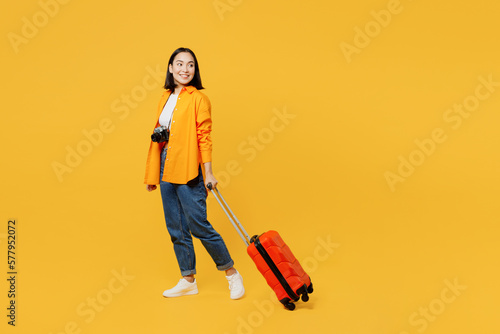 Young woman wear summer casual clothes walk go with suitcase bag look aside isolated on plain yellow background. Tourist travel abroad in free spare time rest getaway. Air flight trip journey concept.
