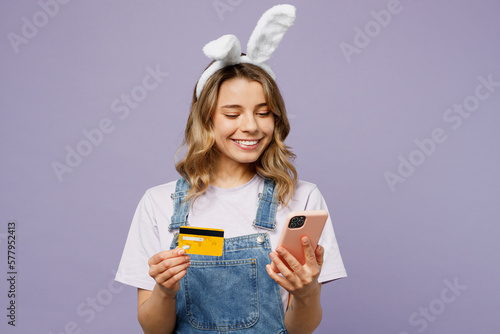 Photography Young fun woman wearing casual clothes bunny rabbit ears using mobile cell phone credit bank card shopping online order delivery isolated on plain pastel light purple background Happy Easter concept