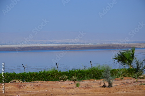 Panoramic view of the beautiful, clear blue Dead Sea shimmering and shining on a bright sunny day in Jordan and the dry land around it.