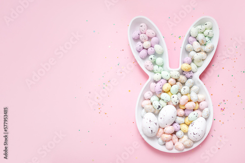 
spring easter layout. bunny plate with easter painted eggs and confetti on a pastel pink background. top view. copy space. flat lay. place for text.