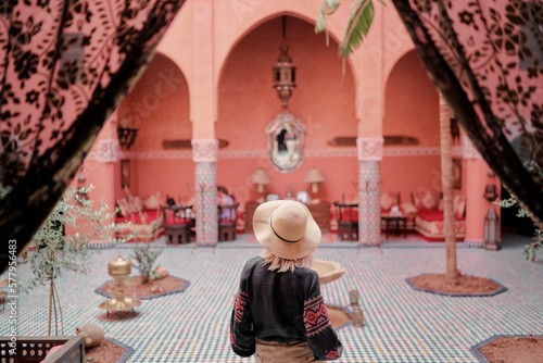 Traveling by Morocco. Happy young woman in hat relaxing in traditional riad interior in medina.