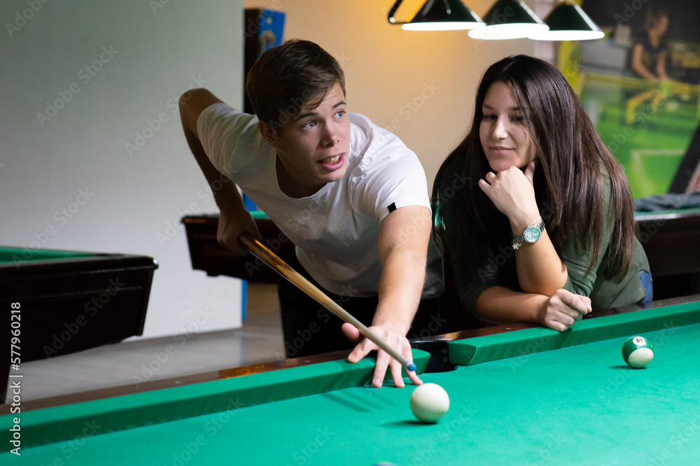 Fototapeta premium A guy and a young and beautiful woman are playing billiards in a club